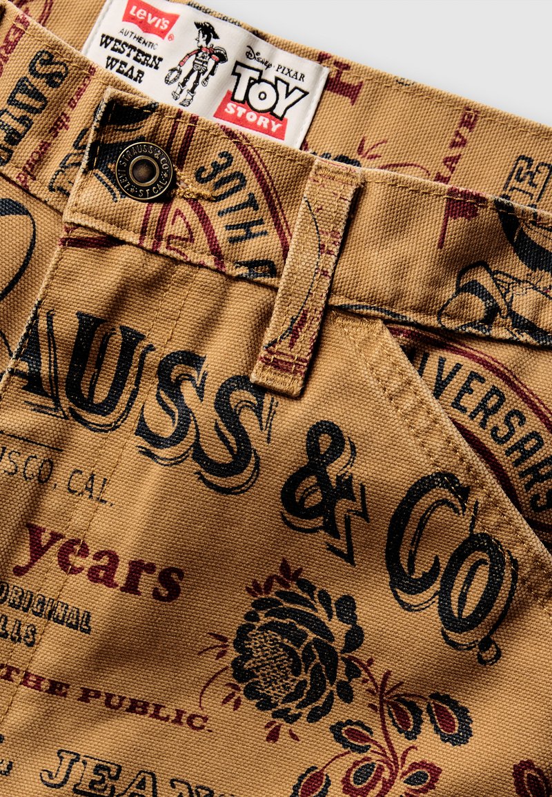 Sandfärgade shorts med svart och röd tryckt text samt blommönster. Innehåller en Levi's-label och detaljer med metallknapp.