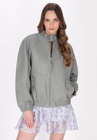 Giubbotto bomber in pelle grigia con zip frontale, polsini a coste, colletto alto e superficie texture. Indossato sopra una leggera gonna floreale a volant.
