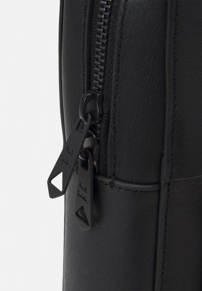 Sort lædertaske sektion med en glat overflade, lynlås med dobbelt sorte træk, og præget logo detaljer på lynlås tags.