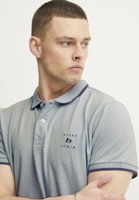 Grå polo skjorte med mørkeblå detaljer, korte ermer og brodert logo på brystet. Glatt tekstur med klassisk krage design.
