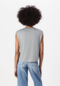 Gray sleeveless t-shirt with a rounded neckline, slightly cropped fit, and soft texture. Paired with light blue wide-leg jeans.