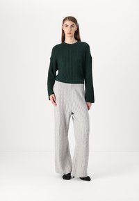 Maglione a costine verde scuro abbinato a pantaloni larghi in maglia a coste grigio chiaro. Entrambi i capi presentano texture morbide e una vestibilità rilassata.