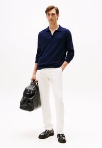 Polo de manga larga azul marino, chinos blancos, zapatos de cuero negros y un bolso de cuero negro. Textura suave, diseño clásico y acentos sencillos.