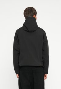 Schwarze Kapuzenjacke mit glatter, matter Textur, im entspannten Schnitt und mit langen Ärmeln, von hinten betrachtet.