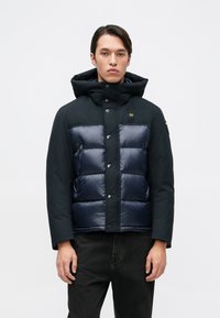 Doudoune noire avec un devant matelassé bleu marine foncé, capuche et fermetures à boutons. Finition lisse avec poches visibles et accent logo.
