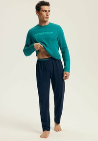 Turkusowa koszula z długim rękawem z napisem "HENDERSON", w połączeniu z granatowymi spodniami na sznurki. Miękka tkanina, luźny krój i wygodny design.