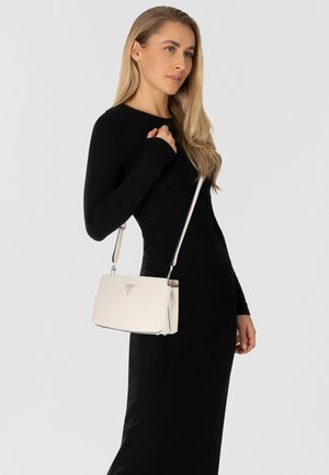 Borsa a tracolla in pelle bianca con logo triangolare dorato, forma strutturata e tracolla regolabile, abbinata a un vestito nero aderente.