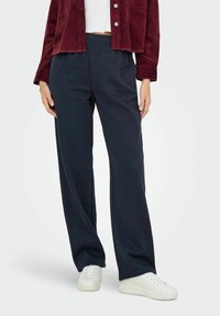 Navy wijdse broek gemaakt van zachte stof met een elastische tailleband, gecombineerd met een cropped kastanjebruine corduroy jas en witte sneakers.