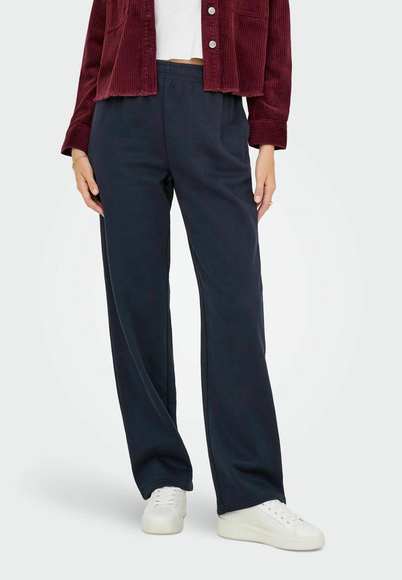 Navy wijdse broek gemaakt van zachte stof met een elastische tailleband, gecombineerd met een cropped kastanjebruine corduroy jas en witte sneakers.