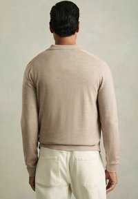 Suéter de manga larga beige con cuello, hecho de un tejido suave. Textura lisa, forma ajustada y diseño minimalista. Vista trasera que muestra las costuras.