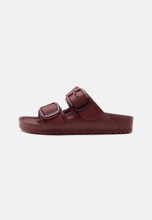 Σκούρο κόκκινο σανδάλι slip-on με δύο ρυθμιζόμενους ιμάντες με αγκράφες και ανάγλυφη σόλα, εμφανίζεται σε πλευρική προβολή σε απλό φόντο.