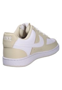 Zapatillas de cuero beige y blancas con un acabado suave, forma redondeada, suela blanca y lengüeta texturizada con cordones; cuenta con un destacado logo de Nike.
