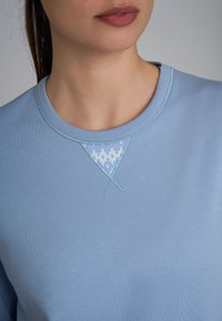 Felpa azzurra con scollo rotondo, dotata di un inserto a motivo triangolare e dettagli di cucitura a contrasto. Tessuto morbido.