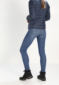 Mörkblå puffjacka, slim-fit blå jeans med subtil sömnad, och svarta ankelbooties med en texturerad yta och snörning.