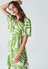 Zelené a bílé vzorované šaty s krátkými rukávy, zapínání na knoflíky, s volným střihem a výrazným listovým vzorem.