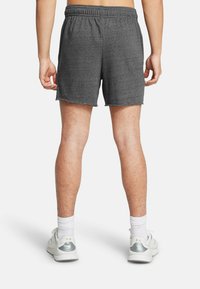 Grå träningsshorts med elastisk midja, med en strukturerad tygart och rå kant. Matchas med vita träningsskor och strumpor.