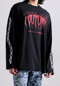 Mustat pitkähihaiset t-paidat, joissa on punainen graafinen teksti ja valkoinen ketjumalli hihoissa. Valmistettu pehmeästä materiaalista, rentoa mallia.