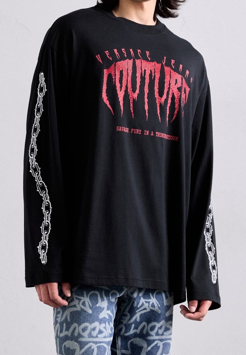 Mustat pitkähihaiset t-paidat, joissa on punainen graafinen teksti ja valkoinen ketjumalli hihoissa. Valmistettu pehmeästä materiaalista, rentoa mallia.