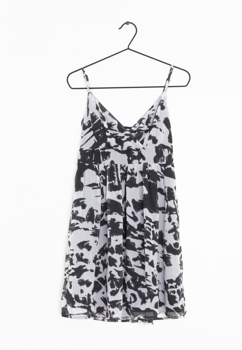 Robe sans manches à motif abstrait noir et blanc, col en V et jupe plissée, suspendue sur un cintre en fil de fer noir.