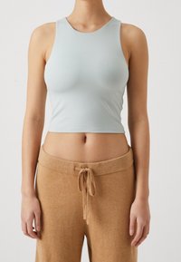 Woman wearing a light blue sleeveless crop top and high-waisted brown drawstring pants against a plain background.