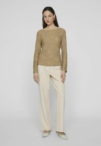 Top lungo a maniche lunghe di colore khaki con scollatura a barca, abbinato a pantaloni a gamba larga di crema e ballerine verde chiaro a punta. Design semplice e moderno.