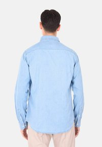 Camicia di jeans azzurro chiaro con maniche lunghe, polsini abbottonati e colletto. Tessuto liscio, fondo curvo e dettagli nella zona dello yoke posteriore.