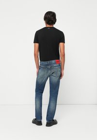 Musta slim-fit t-paita, siniset farkut kevyellä kulutuksella, punainen logotarra takana ja mustat kengät. Yksinkertainen muotoilu ja rento tyyli.