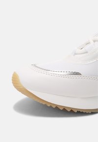 Sneaker bianco con una parte superiore in sintetico liscio, dettagli argentati, suola testurizzata e design della punta rotonda.