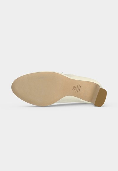 Semelle d'une chaussure habillée couleur crème avec un talon moyen, présentant une semelle en cuir lisse marron clair et un embout de talon en caoutchouc.
