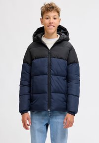 Vattert jakke med svart toppseksjon og mørkeblå nedre del. Har hette, frontglidelås og elastiske mansjetter. Glatt tekstur.