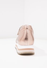 Metalické růžově zlaté tenisky s hladkým svrškem, zipovým uzávěrem a bílou mezipodešví se béžovými a světle hnědými akcenty. Texturovaná podešev.