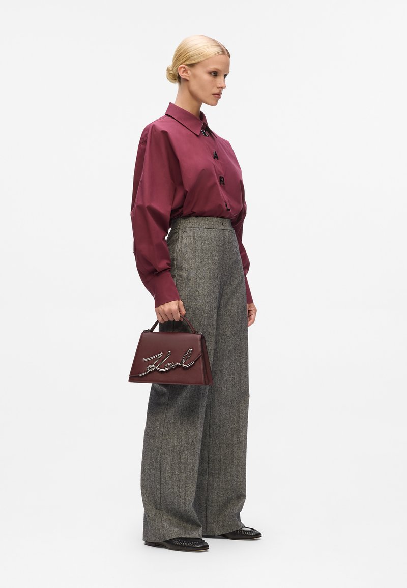 Maroon button-up shirt with glossy fabric, gray plaid high-waisted trousers, and a structured burgundy handbag featuring a metallic logo.