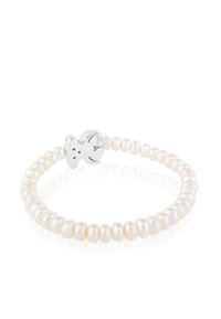 Pulsera de perlas que presenta perlas ovaladas blancas ensartadas con un charm de oso de peluche de plata como pieza central, grabado con el nombre de la marca.