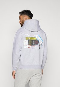 Γκρίζα φούτερ με μεγάλo γραφικό στην πλάτη, που θυμίζει ταμπλό αναχωρήσεων αερολιμένα με εισιτήρια και σφραγίδες διαβατηρίου.