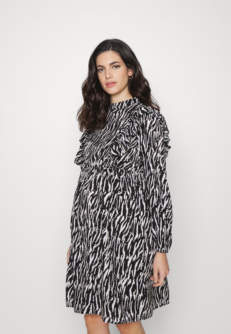 Vestido em preto e branco com padrão, mangas longas, detalhes franzidos nos ombros e uma silhueta de saia plissada.