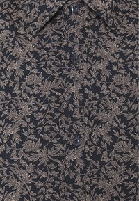 Maglietta nera a maniche corte con un motivo di foglie beige, con chiusura a bottoni e un tessuto morbido e texturizzato.