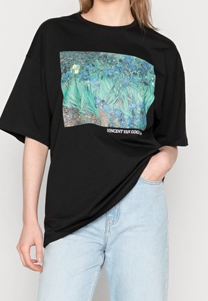 Zwarte katoenen t-shirt met een voorkantafbeelding van blauwe iris, met de tekst "VINCENT VAN GOGH." Oversized pasvorm met korte mouwen.