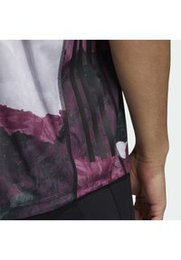 Lila och svart mönstrad sporttröja med en texturerad yta, med tre svarta ränder på sidan och en sydd etikett med texten "AEROREADY."