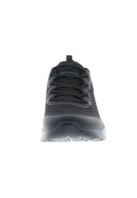 Zapatilla deportiva negra con parte superior de malla, puntera redonda y cordones elásticos. Presenta una suela de goma gruesa y una superficie texturizada en la parte superior.