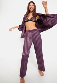 Paarse satin pyjama set met een gestreept ontwerp, bestaande uit een losse shirt en broek met elastische taille. De bh heeft bloemige kantdetails.