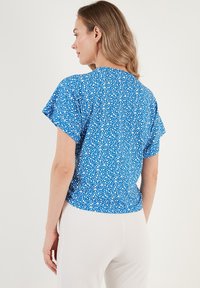Maglietta blu a maniche corte con motivo floreale, scollatura tonda e vestibilità morbida. Tessuto testurizzato con leggero lucido, abbinata a pantaloni bianchi.