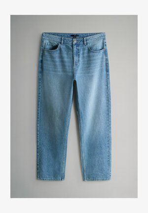 Šviesiai mėlynos spalvos džinsai iš džinsinio audinio su laisvu prigludimu, turintys penkias kišenes, užsegimą su saga ir subtilų audinio išblukimą, išdėstyti ant pilkos spalvos fono.