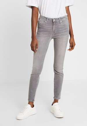 Strakke jeans in lichtgrijs denim met een zachte textuur, voorzien van een ontwerp met vijf zakken en een gulp met knopen. Draagt erbij witte sneakers.