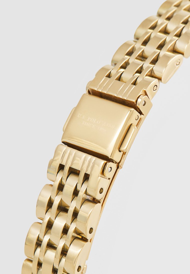 Goldfarbener Edelstahl-Tracker mit einem Gliederarmband, das über eine polierte Oberfläche, einen rechteckigen Verschluss und ein graviertes Markenlogo auf der Rückseite verfügt.