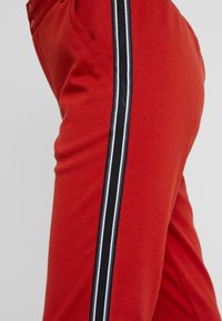 Rode sweatpants met een zachte textuur, voorzien van een zwart-witte zijstreep en een slim fit. Inclusief zijzakken en knoopdetails.