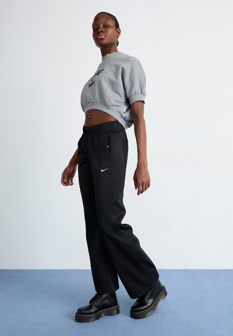 Sweatshirt grigio corto con maniche corte, abbinato a pantaloni neri a sigaretta con tasche laterali e stivali neri con lacci e suole spesse.