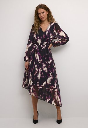 Robe fluide et asymétrique en tissu transparent, ornée d'un motif abstrait violet, noir et blanc, avec des manches longues et une taille cintrée.
