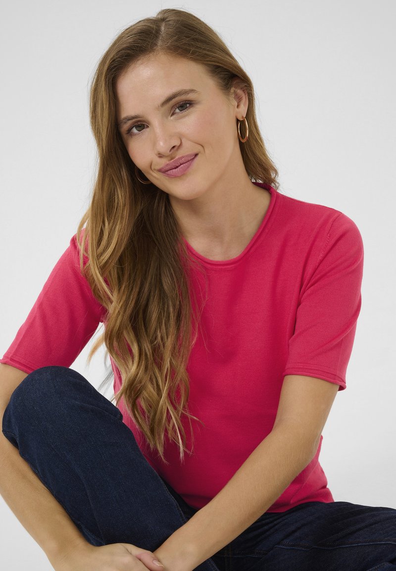 Fitted short-sleeve t-shirt in bright pink cotton with a round neckline, paired with dark denim jeans. Smooth texture, casual design.