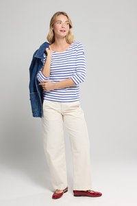 Blauw-wit gestreepte long-sleeve top, gecombineerd met beige wijdpijpen. Rode platte schoenen en een spijkerjack over de schouder gedrapeerd.