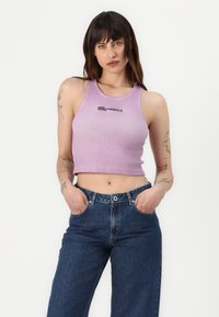 Violets krāsas ribota augsta topa ar apaļu dekoltē un melnu logotipa tekstu, kas apvienots ar augsto jostasvietu tumšās džinsu biksēm. Gluda tekstūra.